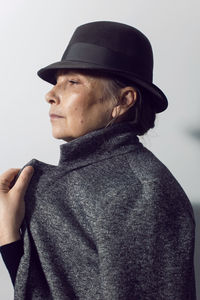 Fashionable older woman in black clothes and a hat stands against a white wall in the office