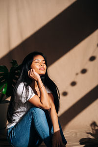 Portrait of young woman sitting against wall