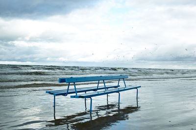 Empty bench at beach against sky