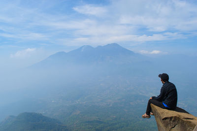 Man sitting on mountain against sky