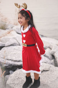 Cute girl wearing red dress and headband standing on rocks