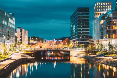 Illuminated buildings by river against sky in city at dusk