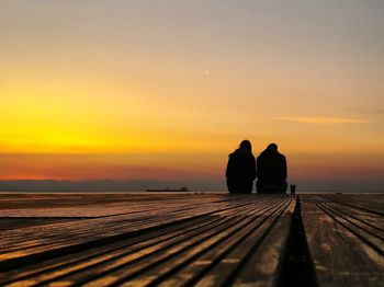 Silhouette people sitting on pier against sky during sunset