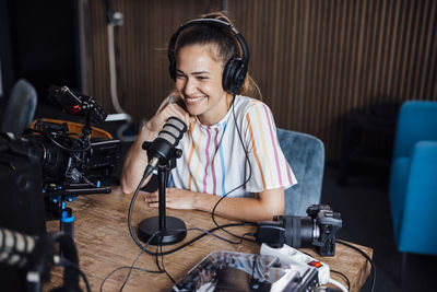 Happy influencer wearing headphones talking into microphone and vlogging in studio