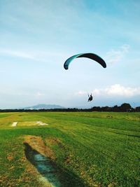 Person paragliding on field against sky
