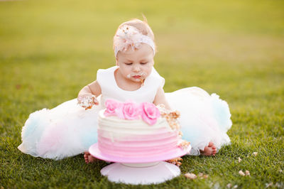 Baby girl 1 year old wear princess dress eating birthday cream cheese cake sitting on grass