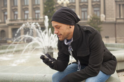 Full length of young man sitting in city during winter