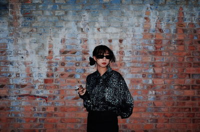 Portrait of a young woman standing against brick wall