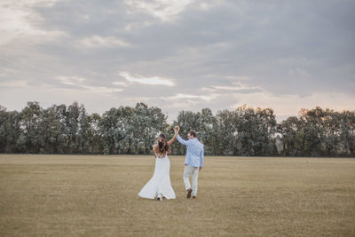 Rear view of bride and groom walking on grassy field