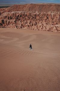 Person walking on sand with rock in background