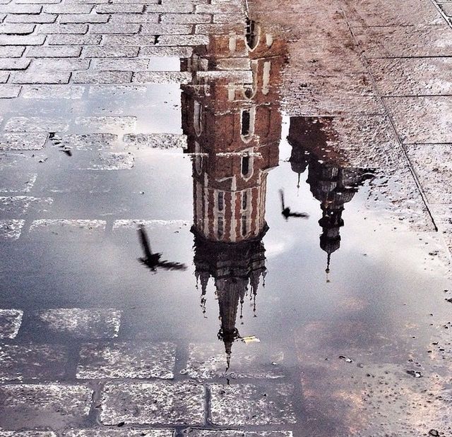 architecture, puddle, water, building exterior, built structure, reflection, wet, street, high angle view, waterfront, rain, city, outdoors, cobblestone, day, standing water, building, travel destinations, sky, paving stone