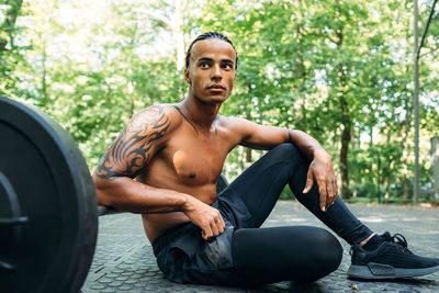 Full length of shirtless young man sitting on footpath