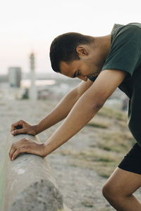 Young male athlete leaning on retaining wall during sunset