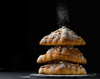 A stack of baked croissants sprinkled with powdered sugar on a black background