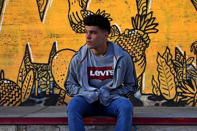 Full length of young man sitting against wall