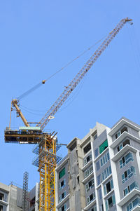 Low angle view of crane by building against clear blue sky