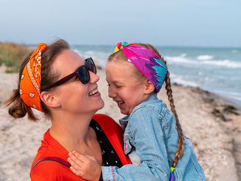 Cheerful mother daughter smiling walking on beach happy family cute child playing rainbow pop it toy