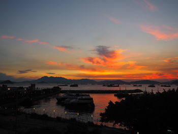 Silhouette city by sea against sky during sunset