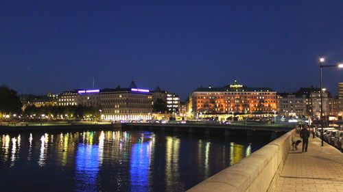 Illuminated city by river against clear sky at night