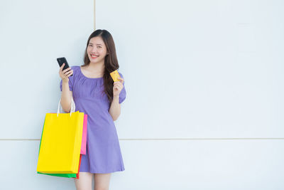 Smiling young woman using phone while standing on wall