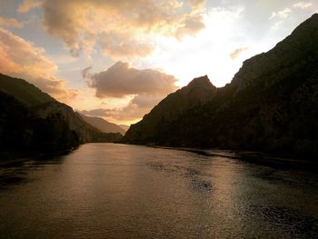 Scenic view of river amidst mountains against sky during sunset