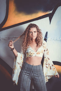 Portrait of young woman standing against wall