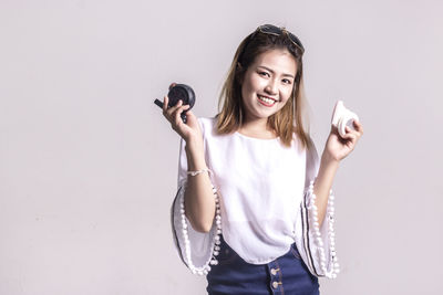 Portrait of woman holding make-up while standing against white background