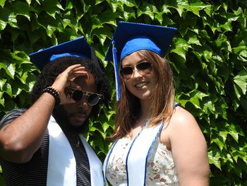 Portrait of friends wearing graduation hats standing against plants