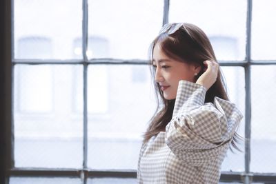 Portrait of young woman looking away while standing against window