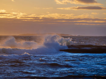 Waves splashing on sea against sky during sunset