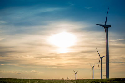 Low angle view of wind turbines on field against sky