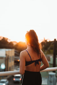 Back view of unrecognizable female in summer outfit standing near railing and admiring sundown while resting in evening city in costa rica