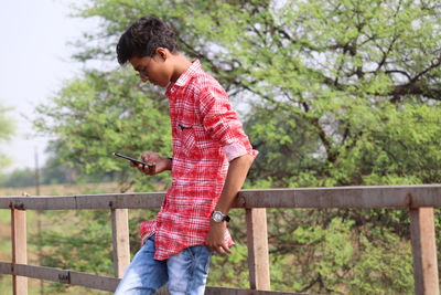 Low section of man holding mobile phone while standing on railing