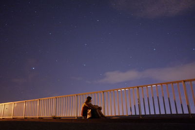 Young woman sitting on bridge at night