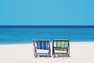 Deck chairs on beach against clear blue sky during sunny day