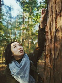 Portrait of beautiful young woman standing by tree trunk