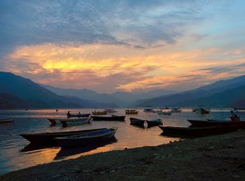 Boats moored in lake against sky during sunset