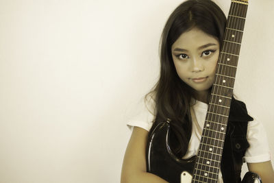 Portrait of young woman holding guitar against wall