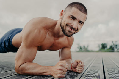 Portrait of shirtless young man exercising on wood