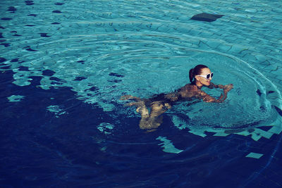 A vintage photo of a woman in a black swimsuit and white sunglasses swimming in the pool