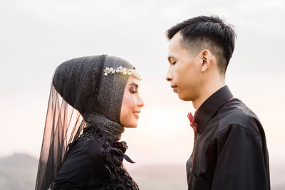 Side view of couple kissing against sky