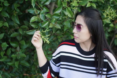 Young woman wearing sunglasses while looking at plant
