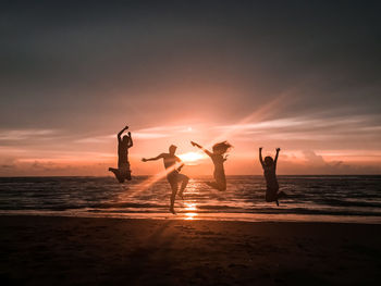 Silhouette people on beach against sky during sunset