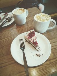 High angle view of cake in plate with fork and coffee cups on table