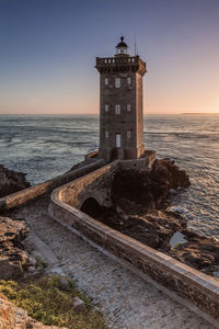 Lighthouse by sea against sky during sunset