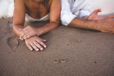 Midsection of couple with rings on sand at beach