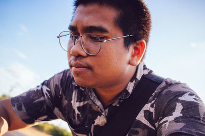 Close-up portrait of young man with eyeglasses against sky
