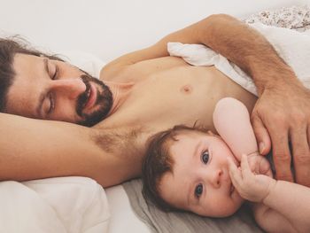 Close-up of shirtless father lying with toddler son on bed