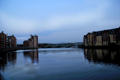Buildings by river against sky in city at dusk