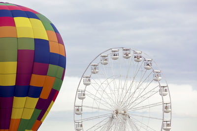 Low angle view of ferris wheel and hot air balloon against sky